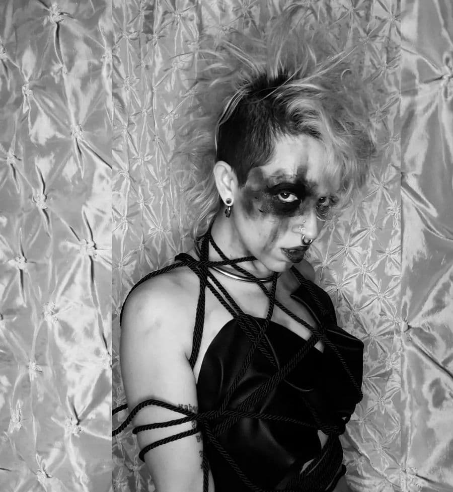 Black and white portrait of Bunny against quilted satin, bound in dark rope, smudged kohl across her eyes.